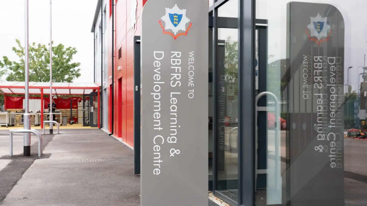 The entrance to the new training centre. There's a glass door on the right hand side, and a sign with the fire service logo on it saying "Welcome to RBFRS Learning & Development Centre".