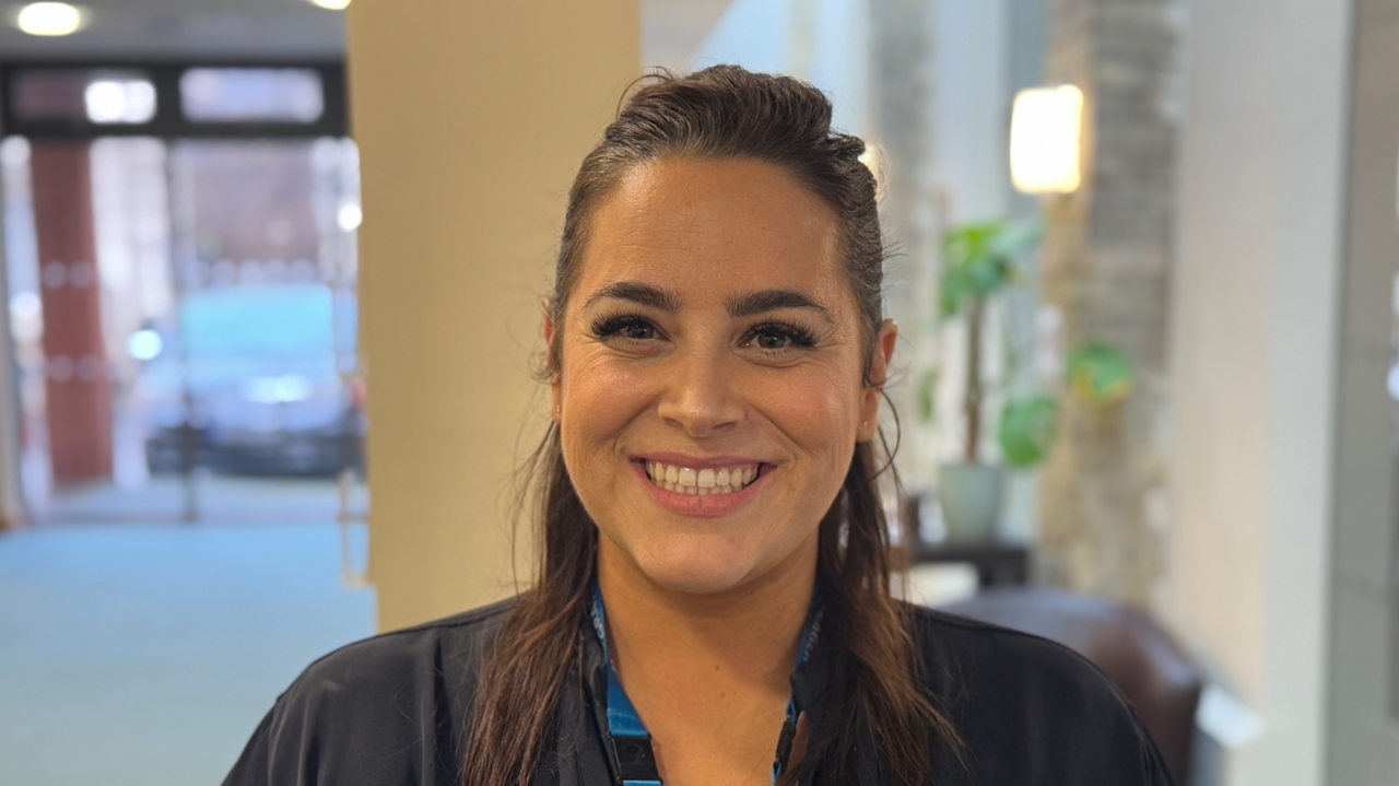 A woman with long brown hair tied back smiling into the camera