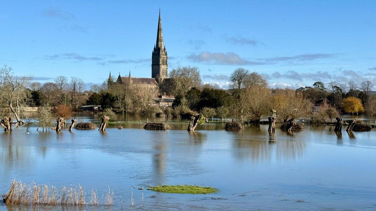 A flooded field with the church and trees in the background against a bright blue sky 