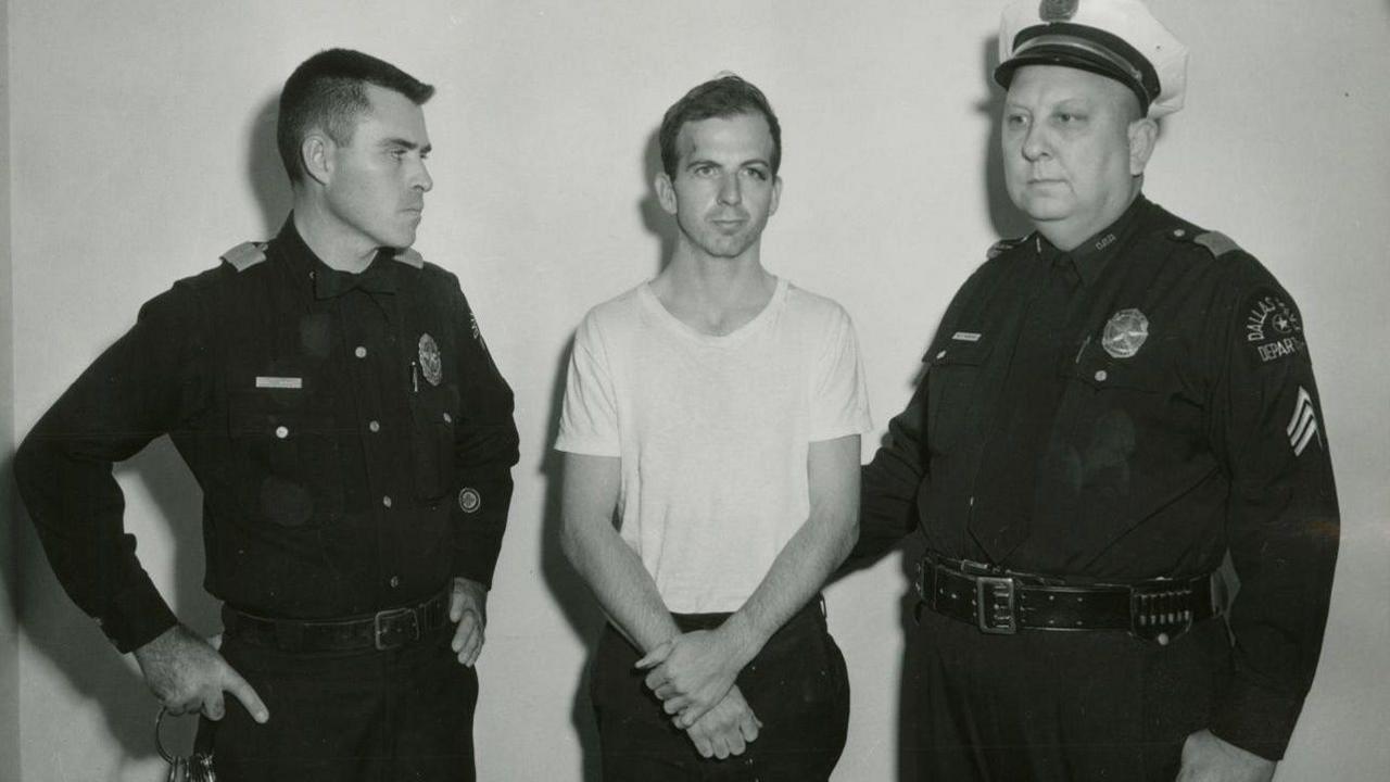 Oswald in a white t-shirt flanked by two police officers in a black-and-white photo