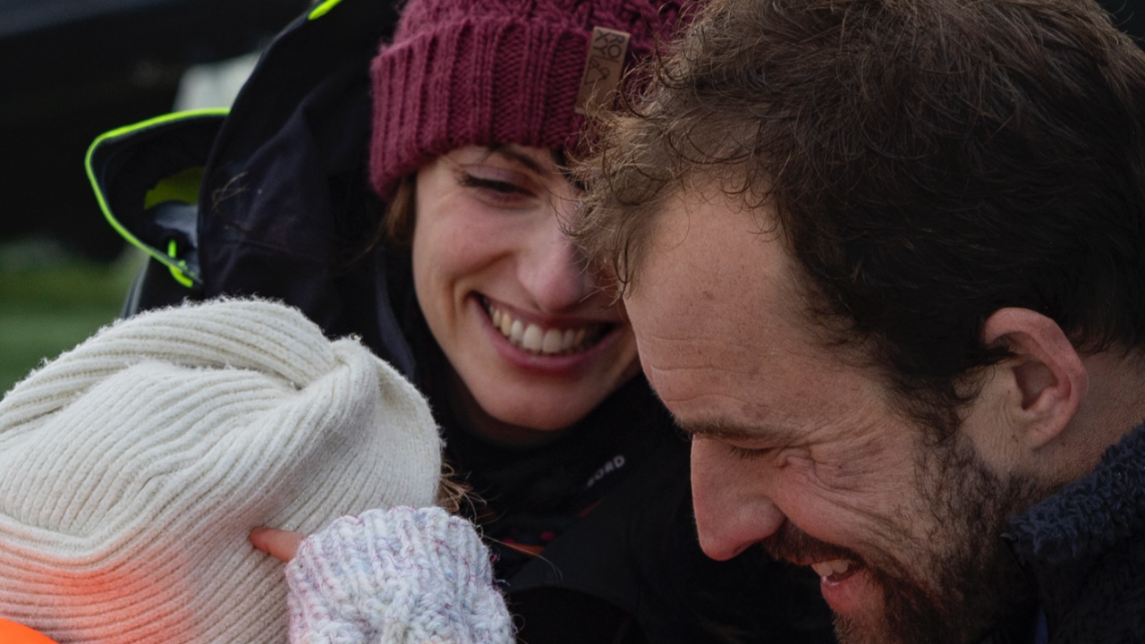 Back view of a small child with a smiling woman and a bearded man.