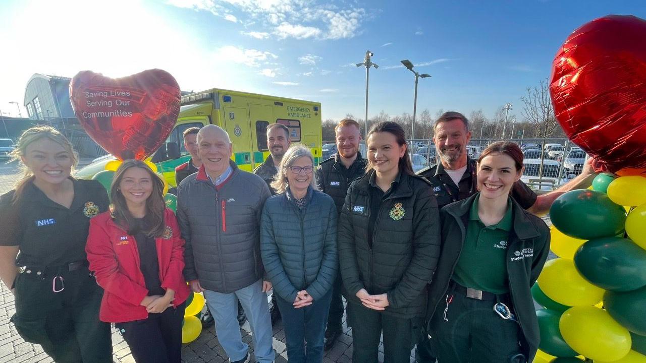 Chris and his wife (centre) pose with Secamb medics in green uniform in front of an ambulance