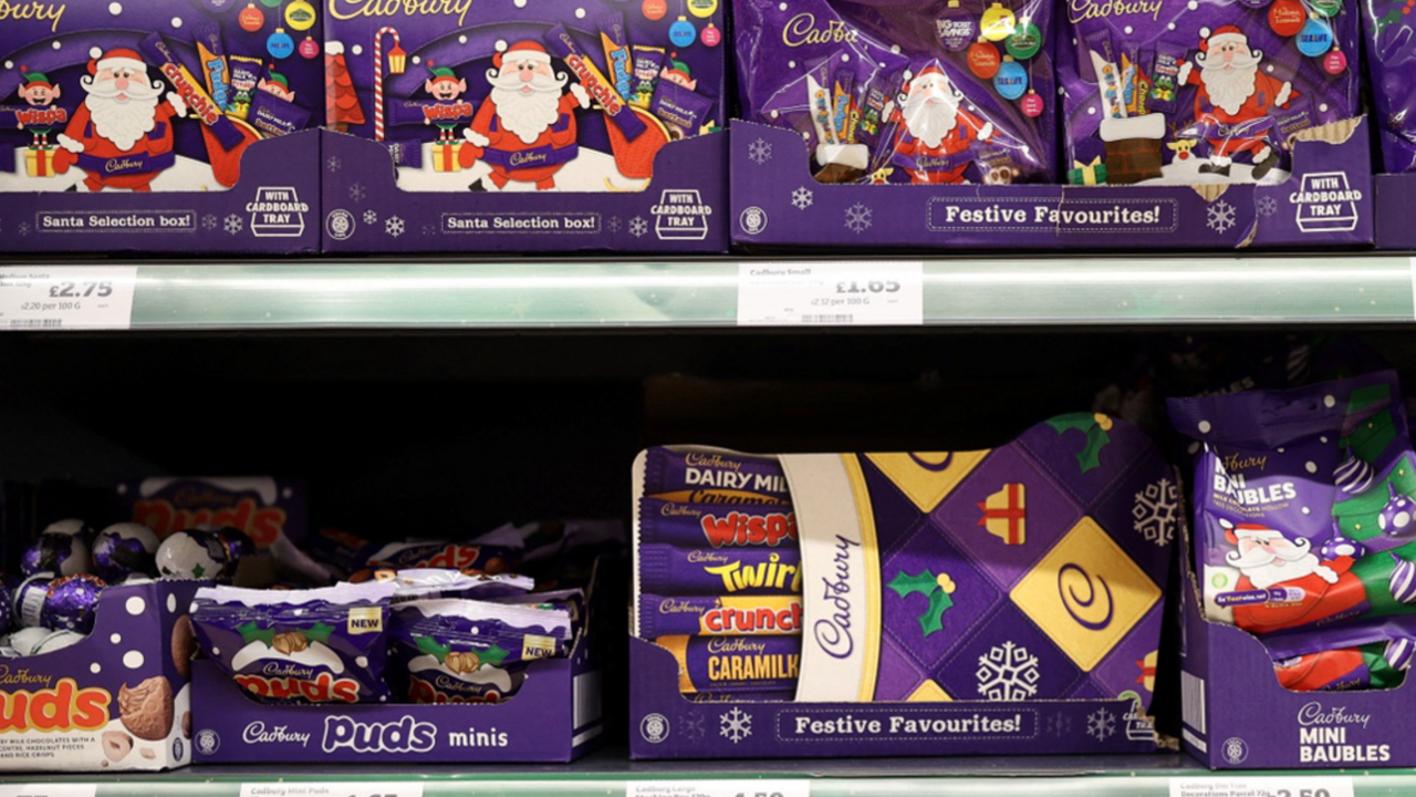 A selection of Cadbury Christmas chocolate is on a shop shelf. It reads: Santa selection box - and has a picture of a Santa and an Elf with pictures of crunchie, fudge, Freddo and other chocolates. 