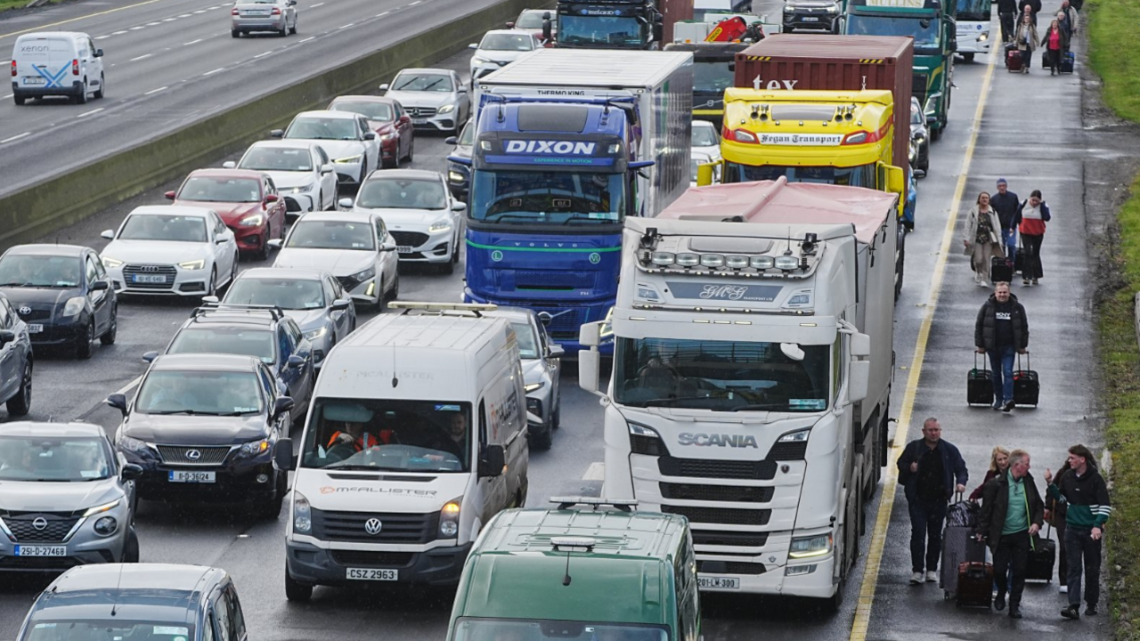 People walk with luggage past heavy traffic on Dublin's M50 - BBC News
