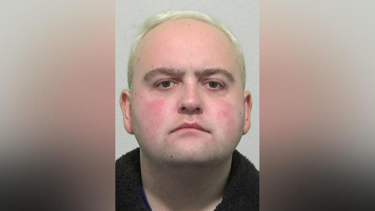 Mugshot of a full-faced man with dyed blond hair.