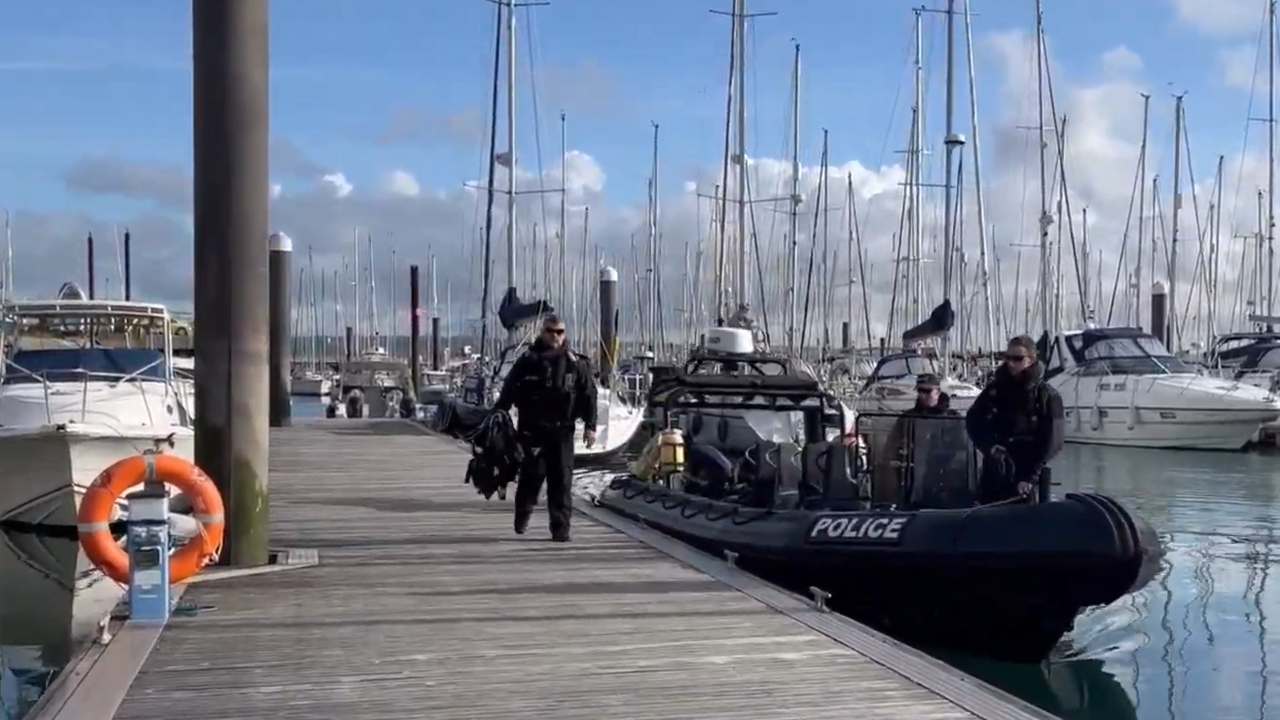 A police boat with uniformed officers in sunglasses is berthed next to a pontoon in Clarence Marina, which is filled with yachts and sailboats.