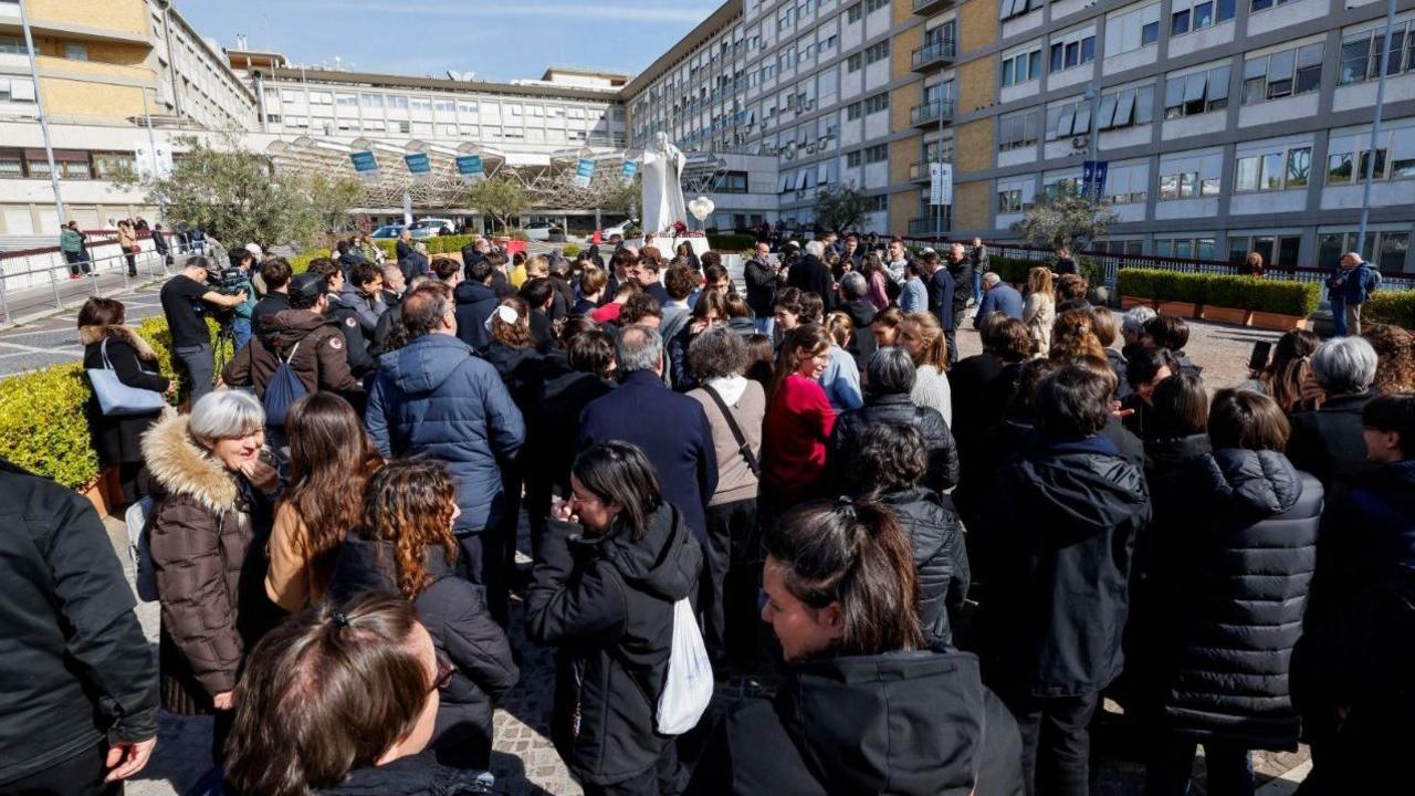 Dozens of people gather outside a statue of late Pope John Paul II outside the Gemelli Hospital where Pope Francis is receiving treatment