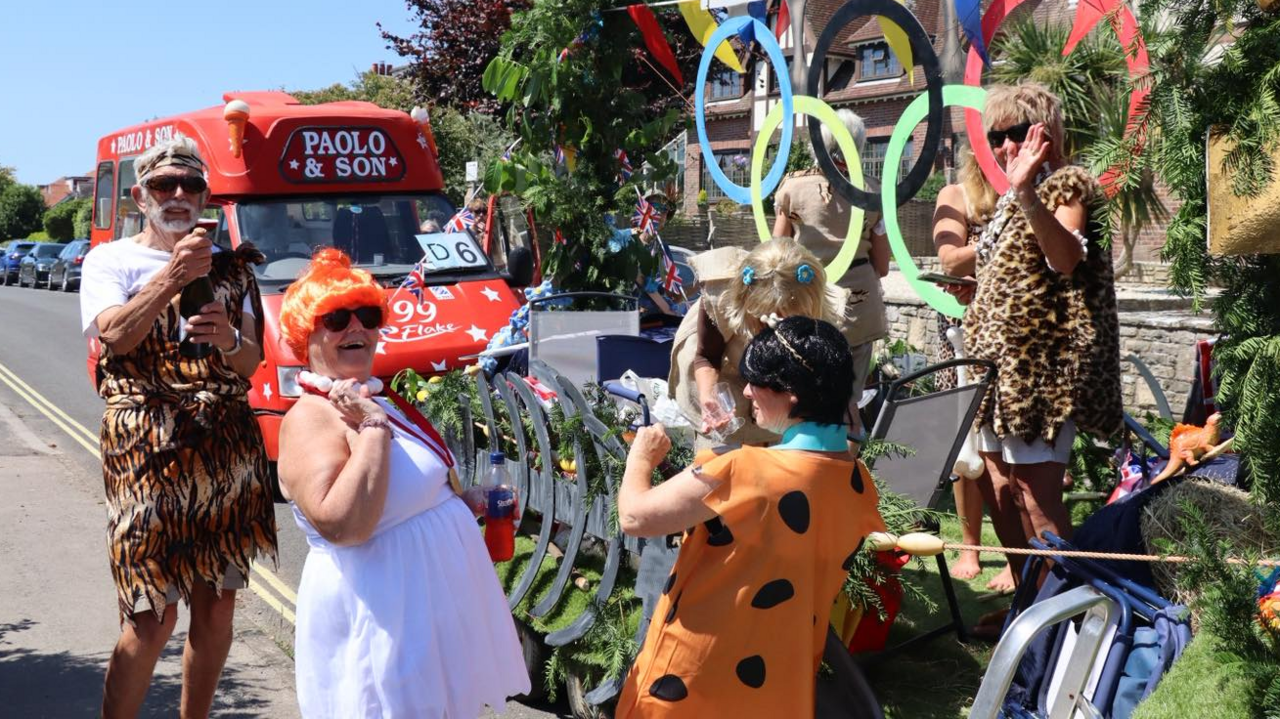 A group of people dressed up as Flintstones characters taking part in the carnival at the weekend, with an ice cream van which says Paolo & Son behind them.