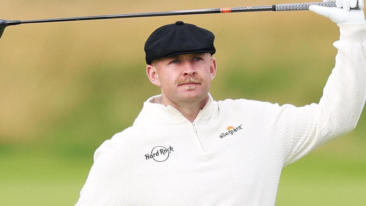 Harry Hall, wearing a flat black cap, with a golf club in his hand