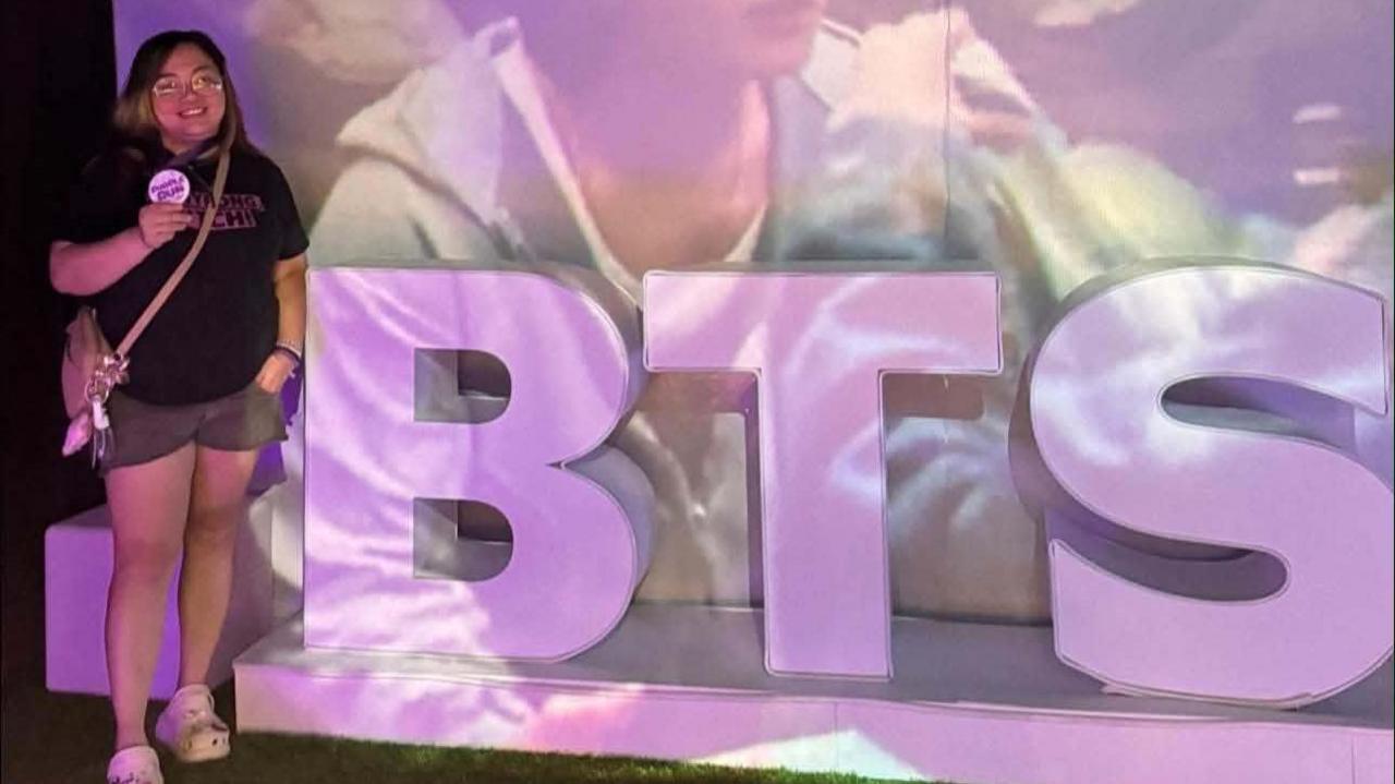 Cookie poses beside a purple BTS signage at an event organised by Army