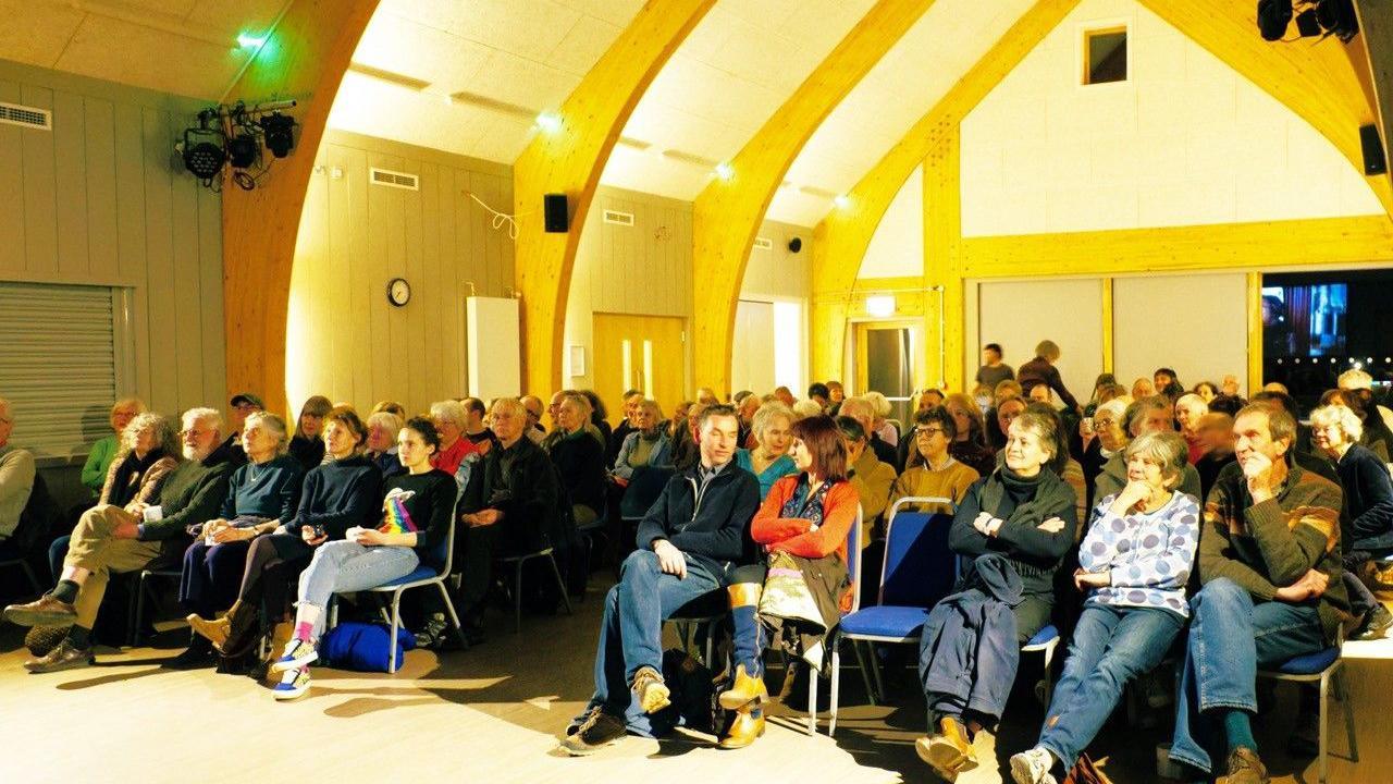 A screening is held in a village hall on moveable chairs set out in rows.