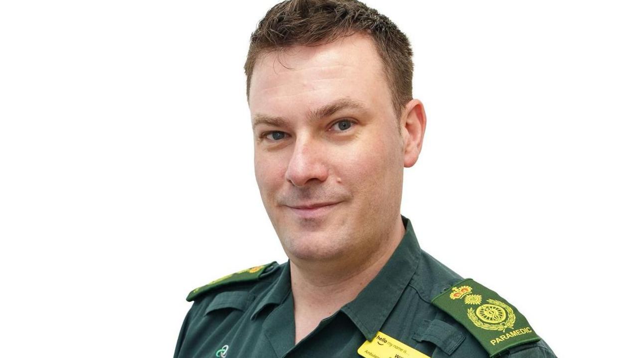 Will Bellamy, a man with short brown hair, he looks at the camera side on, and wears his green uniform.