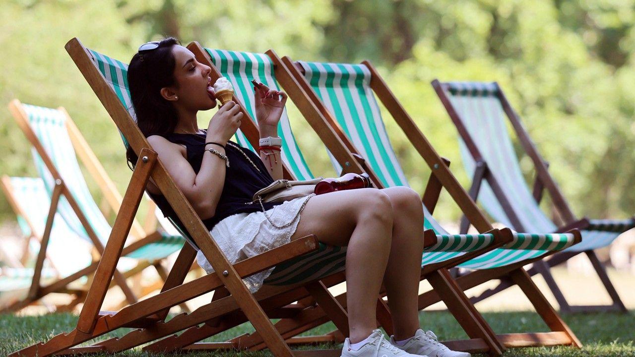 A woman sits on a deckchair the shade while eating an ice-cream at a park in London