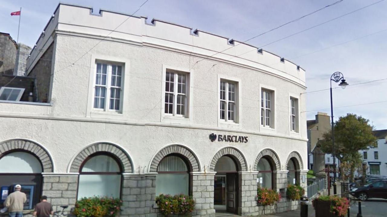 The outside of the building, which is curved and has large arched windows on the ground floor and a castellated roof.
