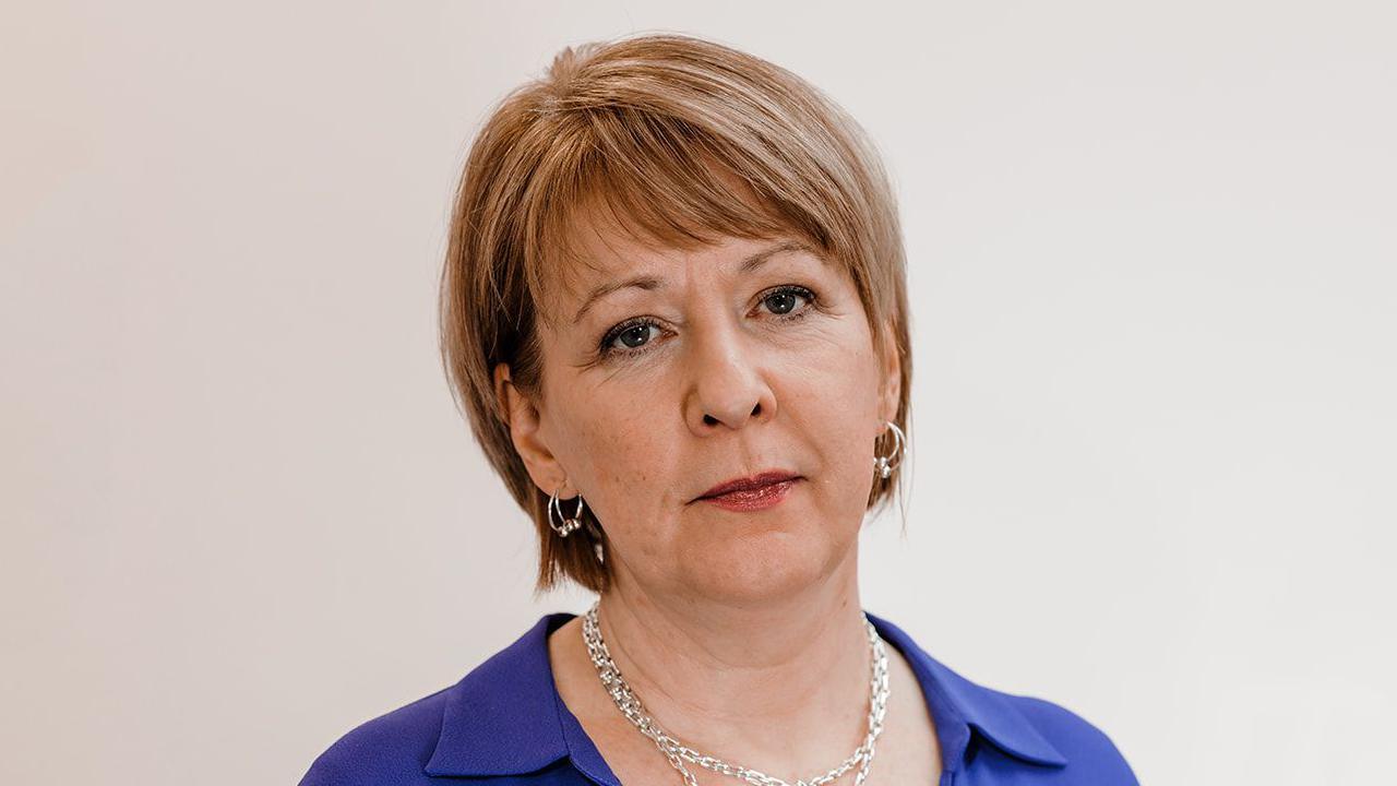 Ashgate Hospice's chief executive officer, Barbara-Anne Walker, a middle-aged white woman with short blonde-brown hair. She is wearing a blue blouse and silver necklaces and silver hoop earrings. She has a serious expression.