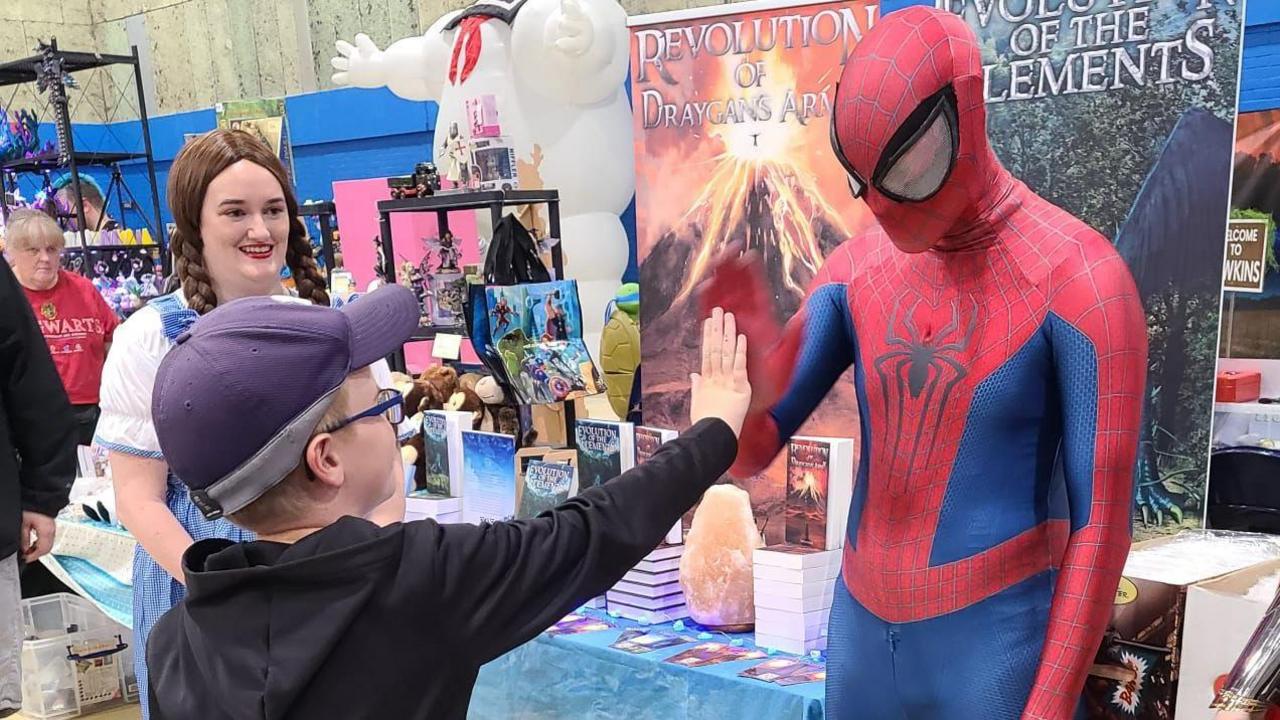 A boy with a black hoody, cap and glasses his high fiving a man dressed as Spider-Man at a convention.