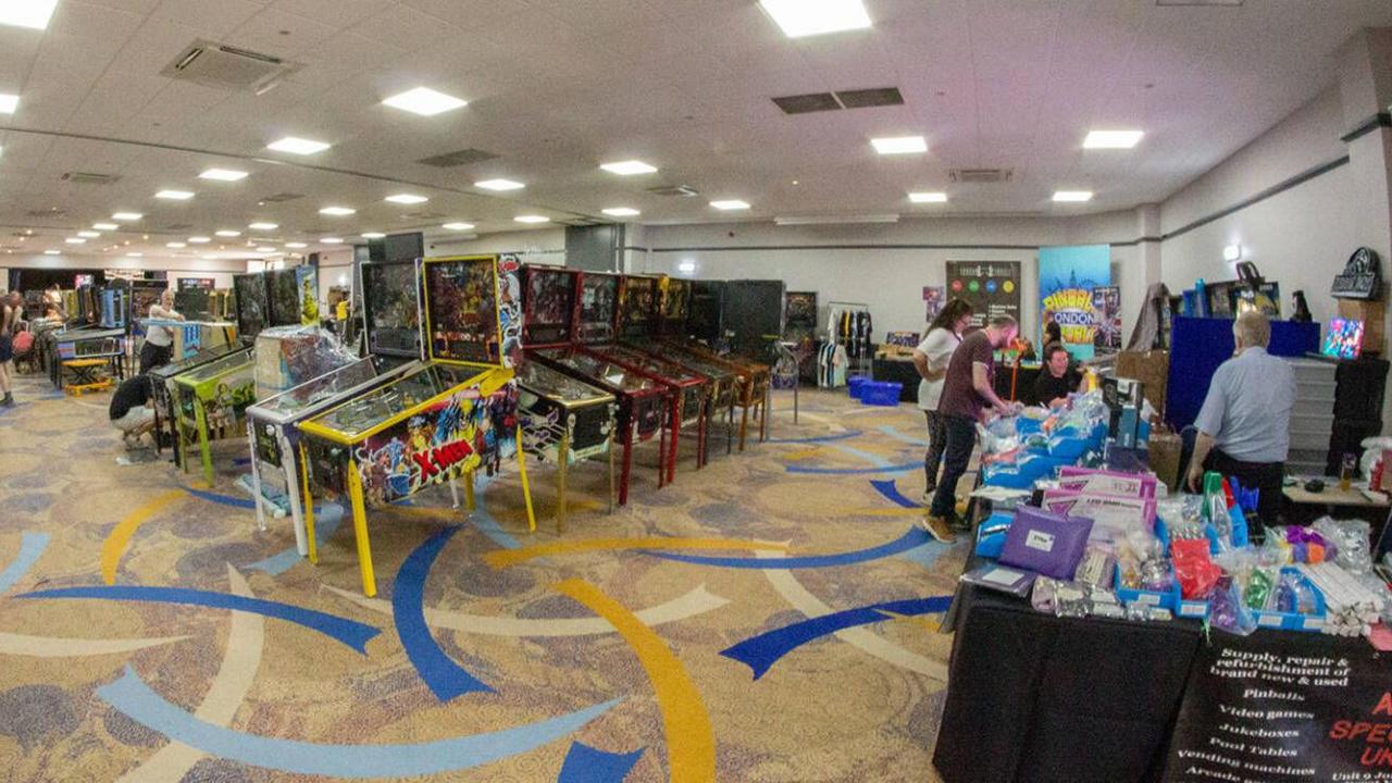 Dozens of pinball machines in the centre of a room and a merchandise stall to the right