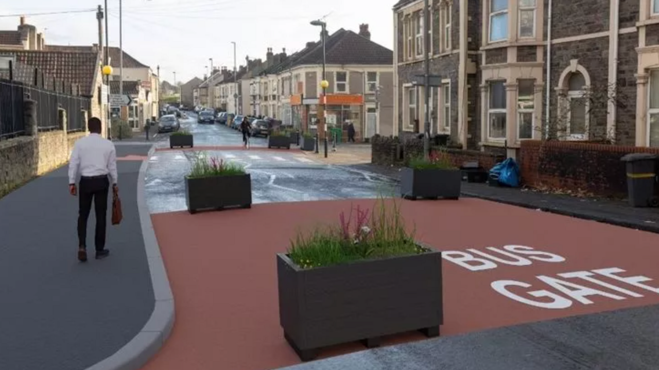 An illustration of flower bed bollards in a former bus gate. There is a pedestrian walking away on the left hand side pavement. Residential homes are pictured on the right of the picture.