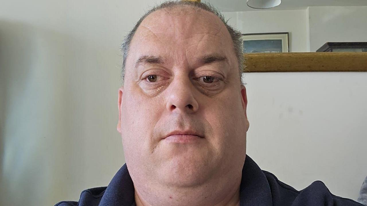 Peter Clarke in a selfie. He has short hair and is wearing a polo top. He appears to be in a domestic setting like a living room or lounge.
