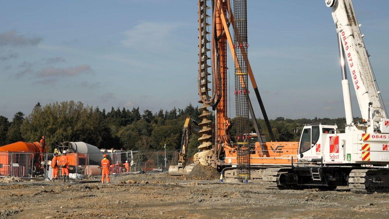 A large bore hole machine being drilled into the ground with workers in high visibility vests looking on 