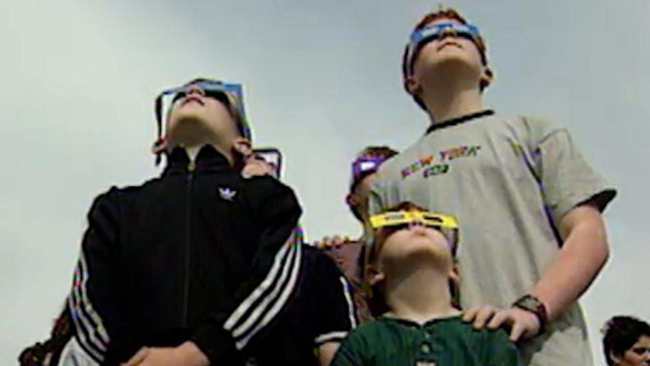 Children wearing solar eclipse glasses and looking towards the sun. 