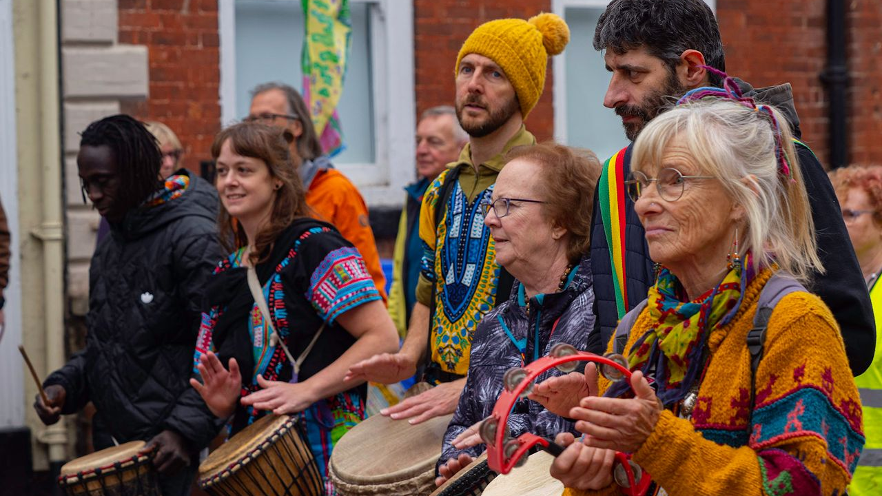 Various people dressed in colourful outfits holding drums