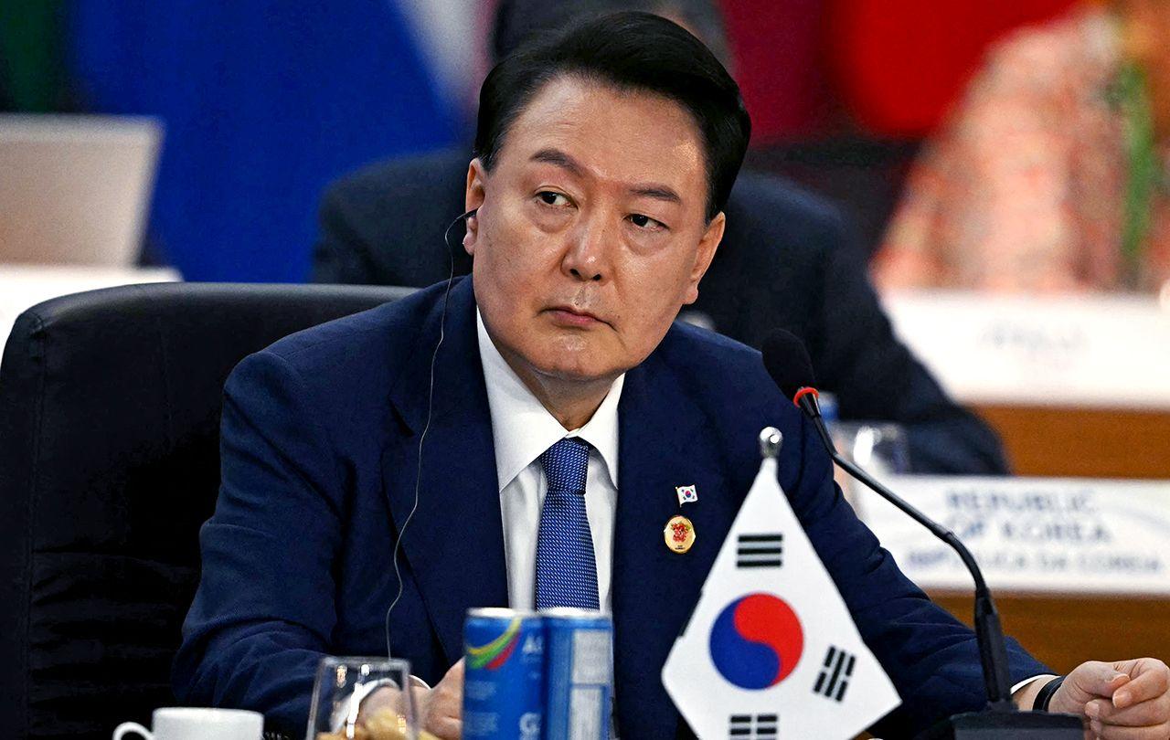 President Yoon Suk Yeol looks away from camera while wearing a suit and tie with an earpiece in, with a miniature South Korea flag and refreshments on the table in front of him as he sits during the third session of the G20 Leaders' Meeting in Rio de Janeiro, Brazil, on November 19, 2024.