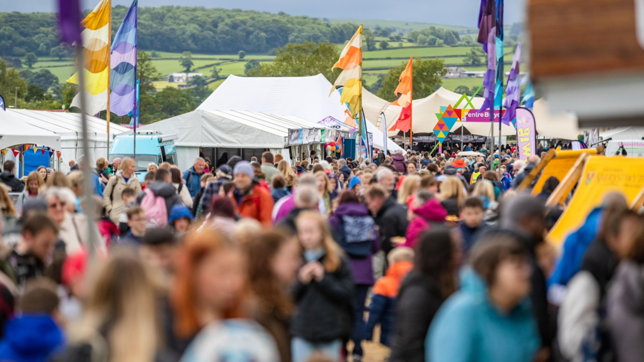 A shot of a crowd at a festival with colourful flags and white tents in the background 