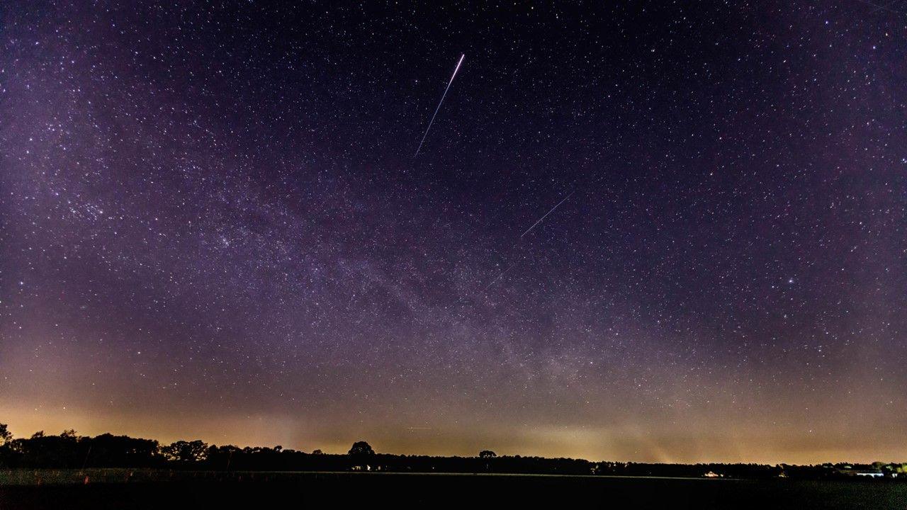 Streaks of light in the sky showing the Lyrids meteors amidst shades of purple and orange in night sky