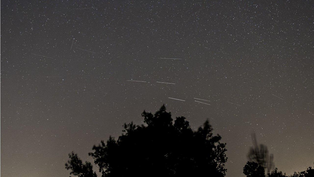 Five white streaks of light of Perseid meteor shower amidst a dark grey sky