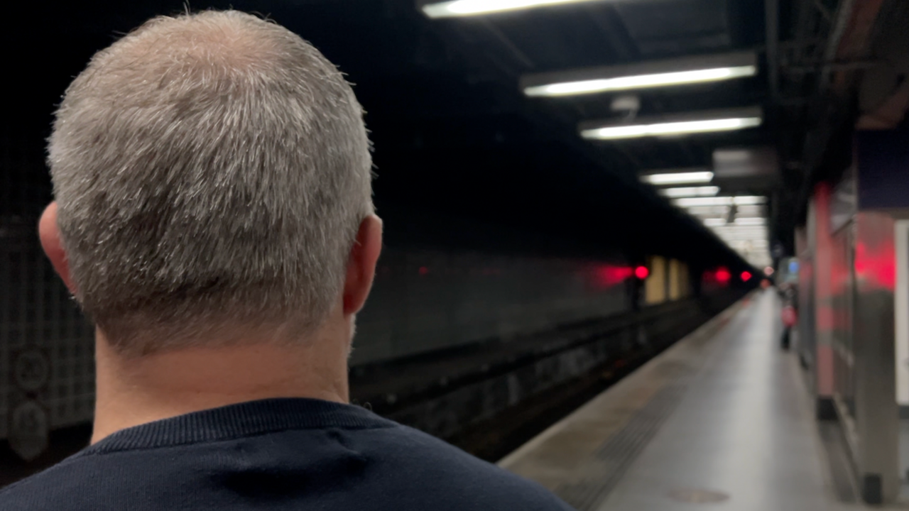 Grey-haired Keith Watson, seen from behind, on the platform of a railway station