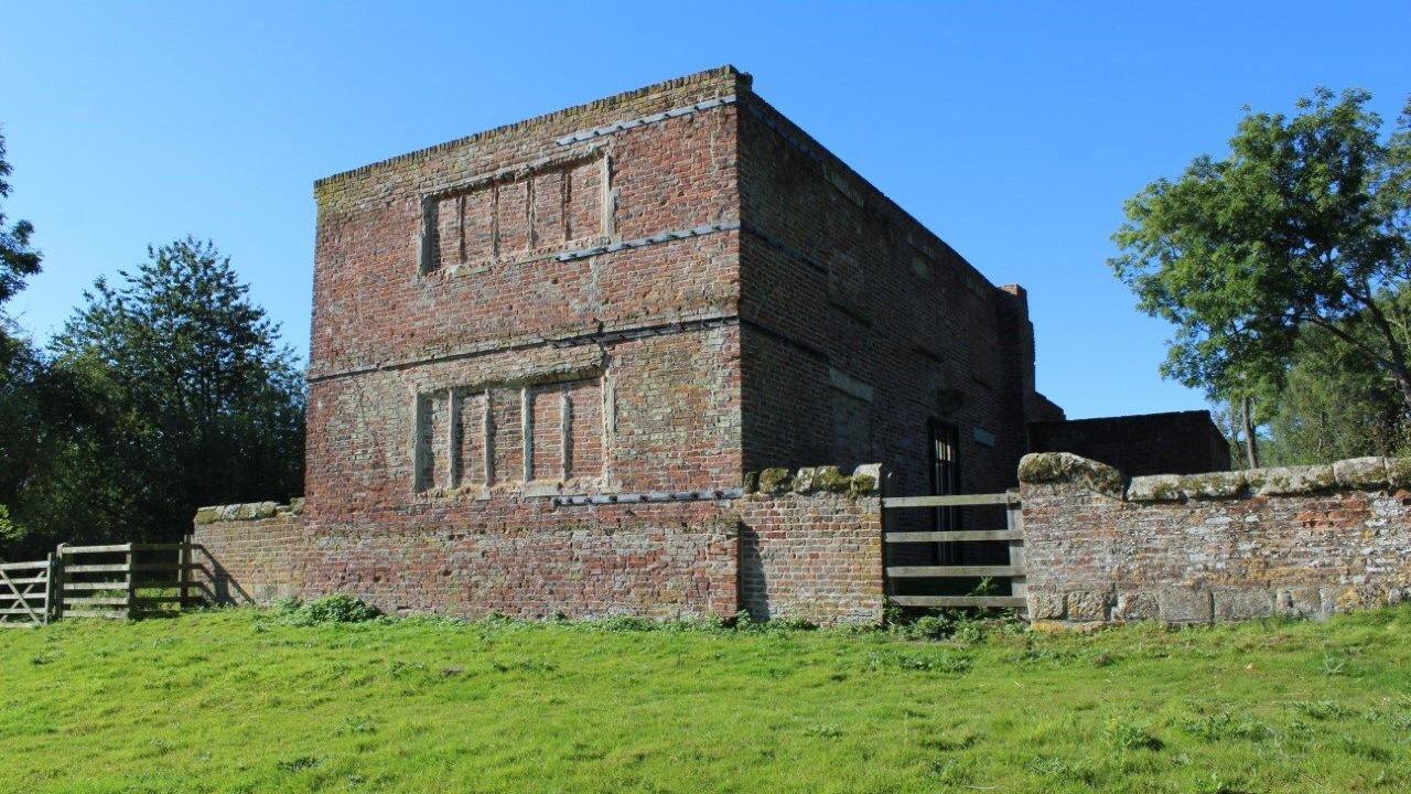 The old brick manor has its windows bricked up and is and is surrounded by gardens and old brick walls.