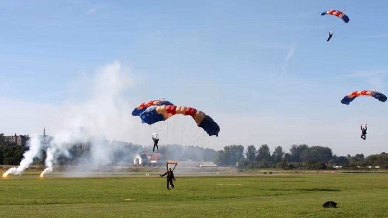 Skydivers land on a green field with red, white and blue parachutes.