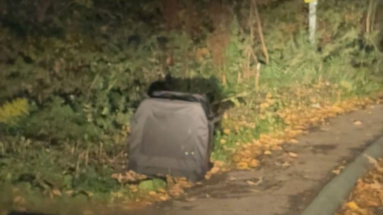 A grey carrier made out of soft material is pictured at the side of a road at night with what appears to be headlights shining at the carrier. 