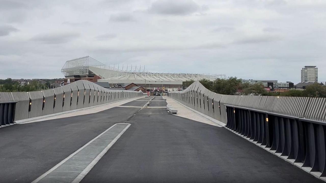 A view of the Stadium of Light from Keel Crossing. It has brick barriers built in an undulating fashion, so they look almost like waves.
