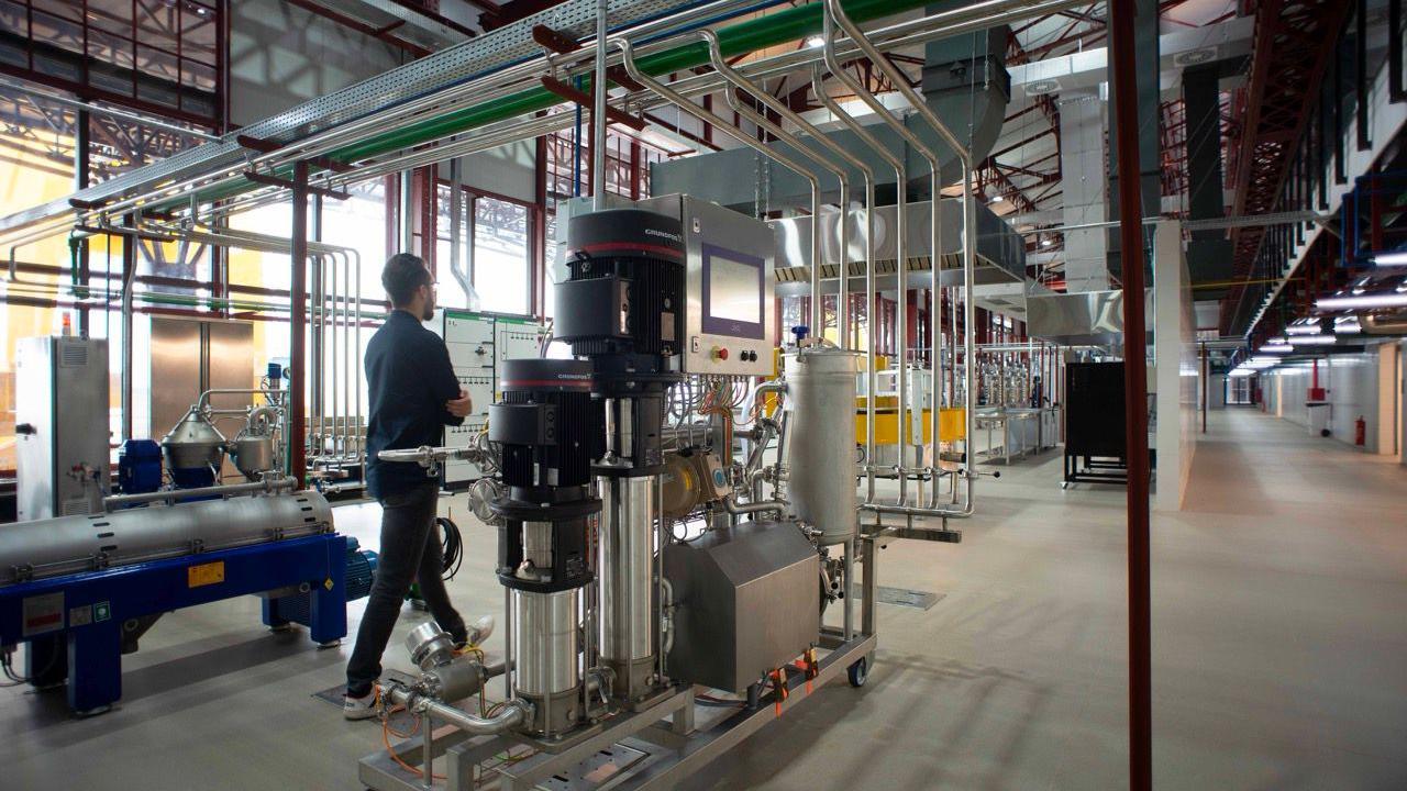 A man walks through a lab with metallic silver machines and pipes in a large room
