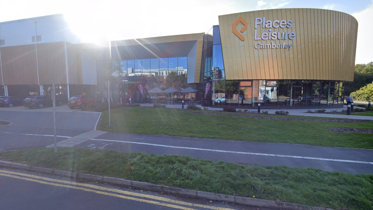 A view of the exterior of Camberley Leisure Centre in Surrey, from the opposite side of the road, with the sun shining over the top of the building.