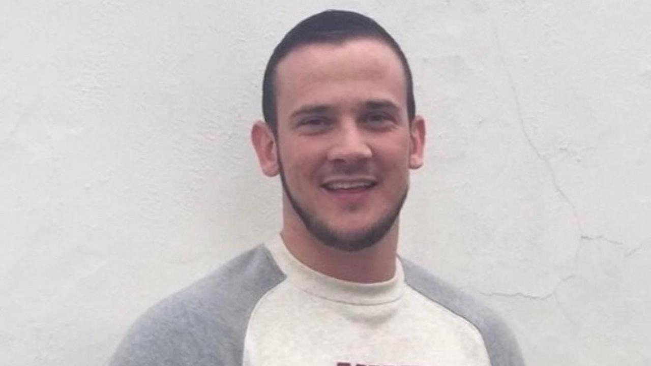Josh Hanson with short brown hair and beard wearing a grey and white top and standing in front of a white wall.