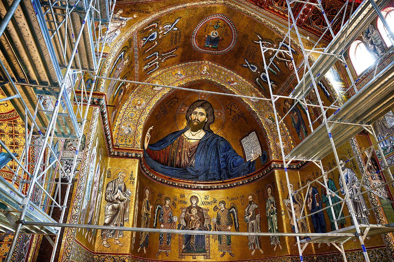 The apse of Monreale's cathedral in Sicily, showing a detailed mosaic of Christ and other religious symbology in mostly gold, with scaffolding in the foreground. 