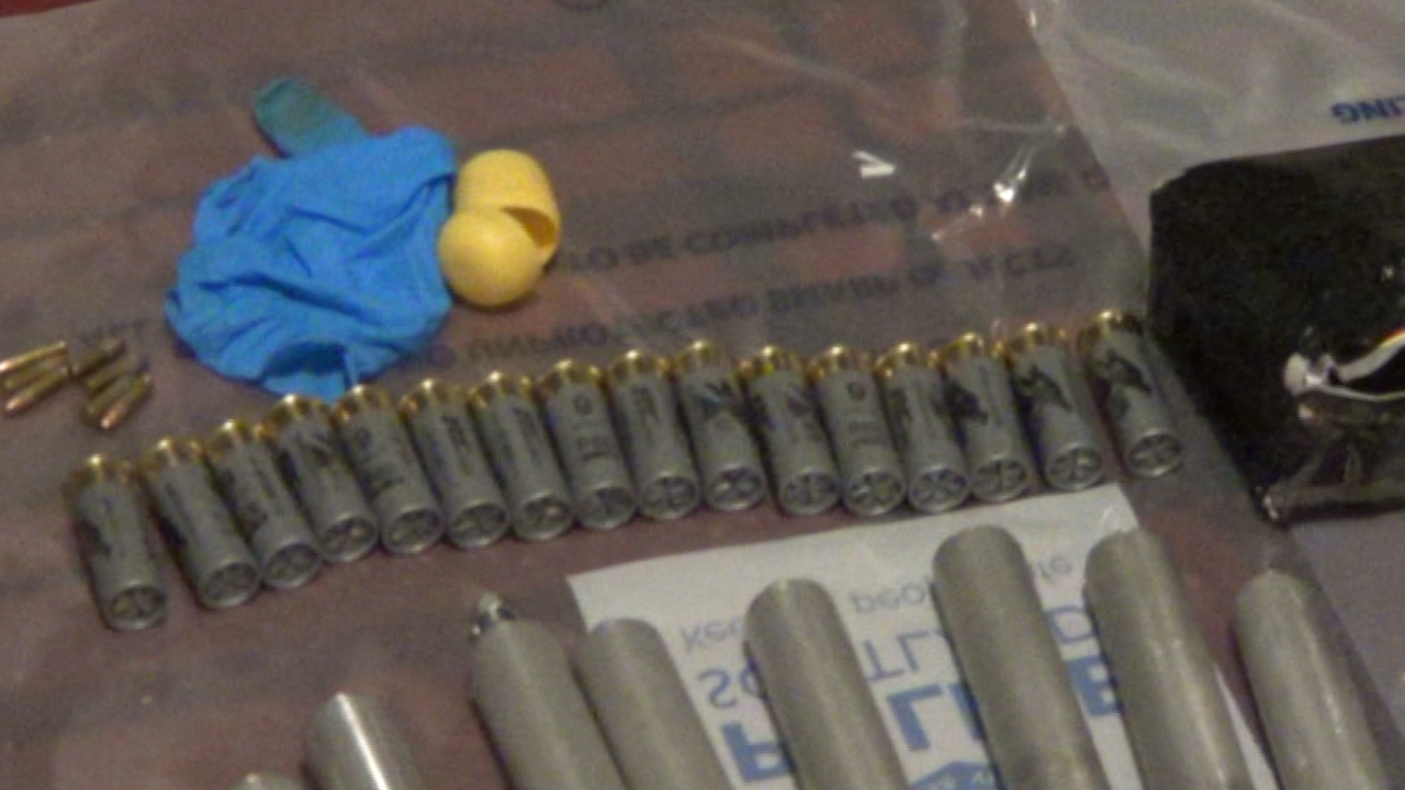 Shotgun cartridges lined up on a table with pieces of metal tubing and blue examination gloves