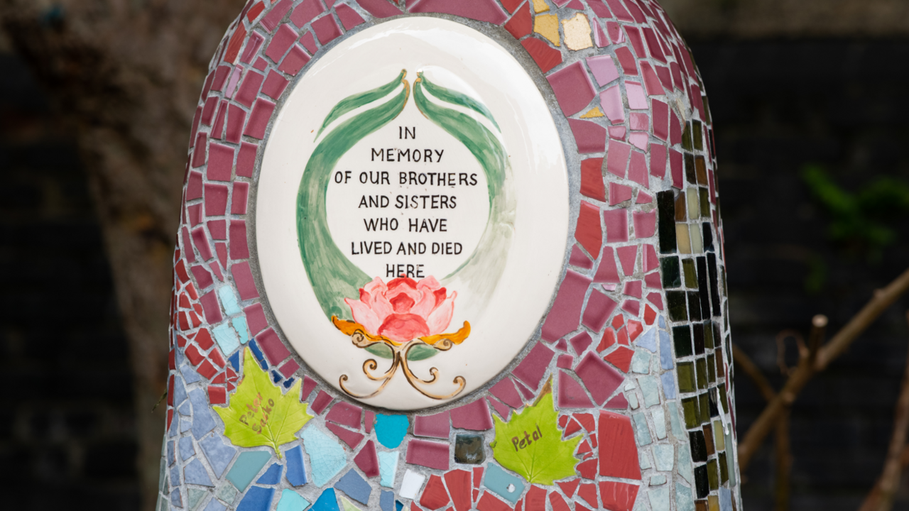 A multicoloured mosaic memorial on a bench erected after residents of cardboard city were evicted. a painted tile in the middle reads, 'in memory of our brothers and sisters who have lived and died here', with leaf tiles underneath containing handwritten names