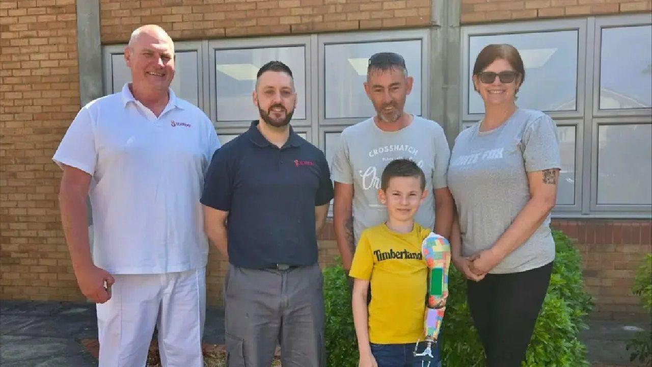 tobi posing with his mum and staff from the prosthetics team