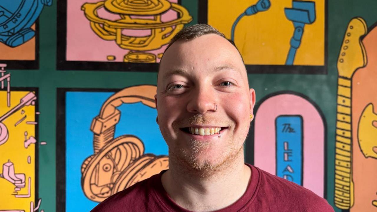 A man smiling at the camera with very short hair and wearing a red shirt