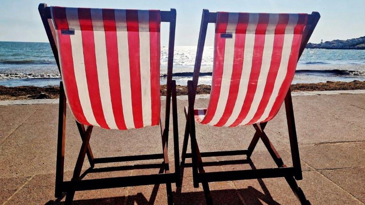 Two red-striped deckchairs on a pathway in front of the beach, sea and hazy blue sky
