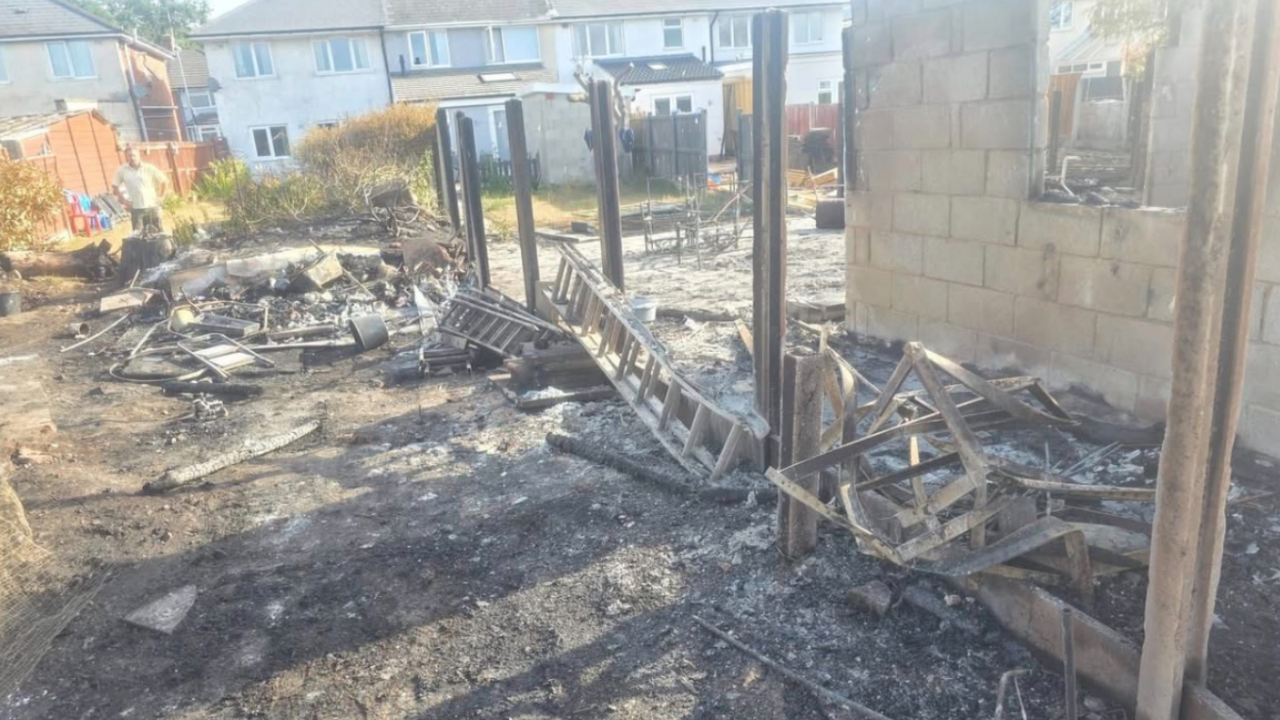 A garden completely destroyed by fire with missing fence panels and debris everywhere. Everything is charred and blackened
