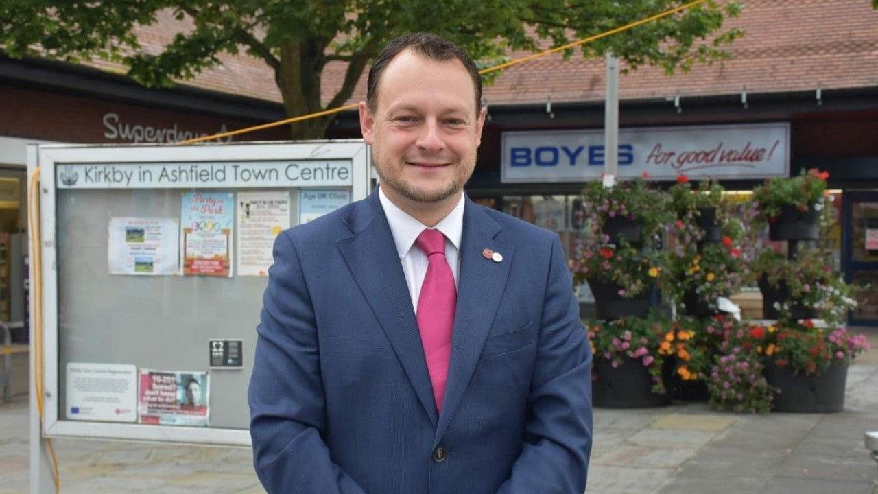 A man wearing a navy suit and a pink tie.