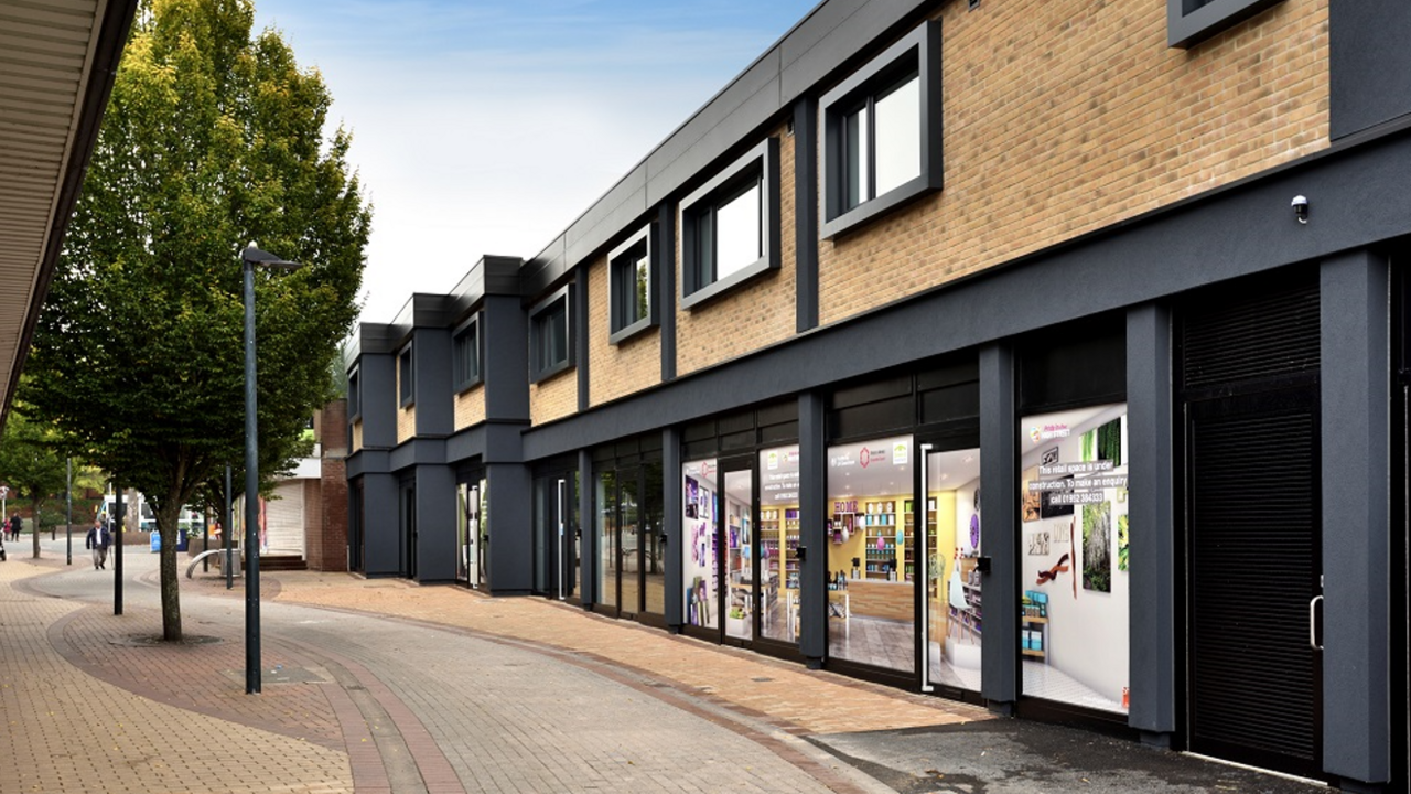 The front of Oakengates theatre with pictures up in the windows of a black-framed beige building and a pavement with trees in front of it