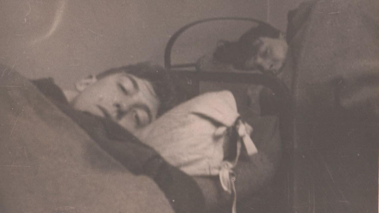 A sepia picture of two soldiers lying in bunk beds looking into the camera