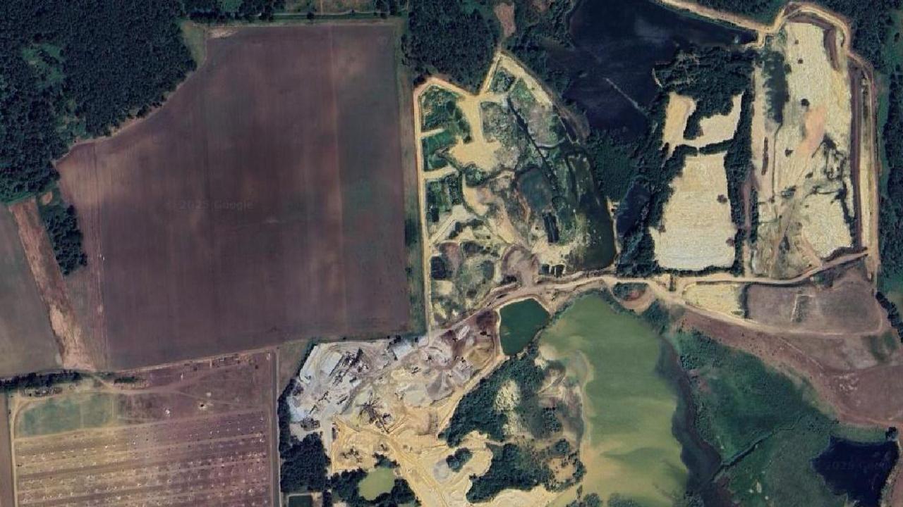 Aerial view of a quarry site and where a proposed solar farm could be built. The image shows green and brown areas, a greenish lake, woodland and roads.