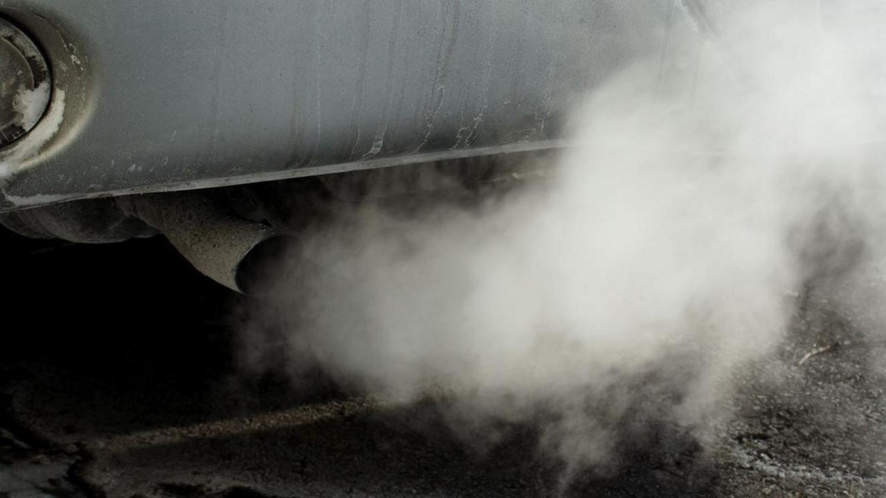 A close-up of a smoky exhaust from a car which has a grey side and looks quite rundown.